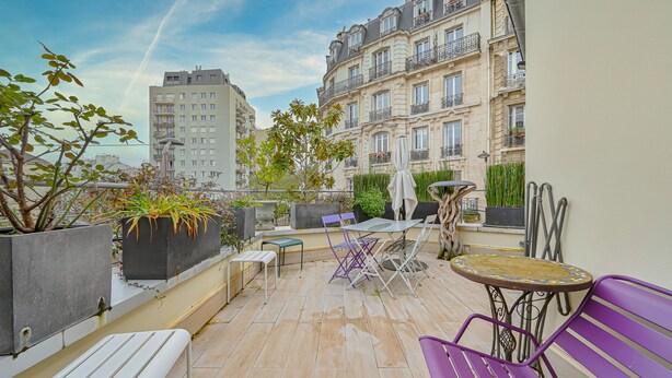 Terraço no telhado com mesa, cadeiras e plantas em vasos.