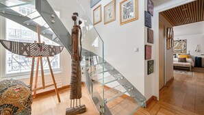 Interior moderno com escadaria de vidro, mobiliário de madeira e obras de arte nas paredes.