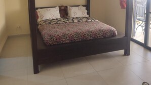 A four-poster bed with a floral bedspread, a red curtain, and a can on a table.