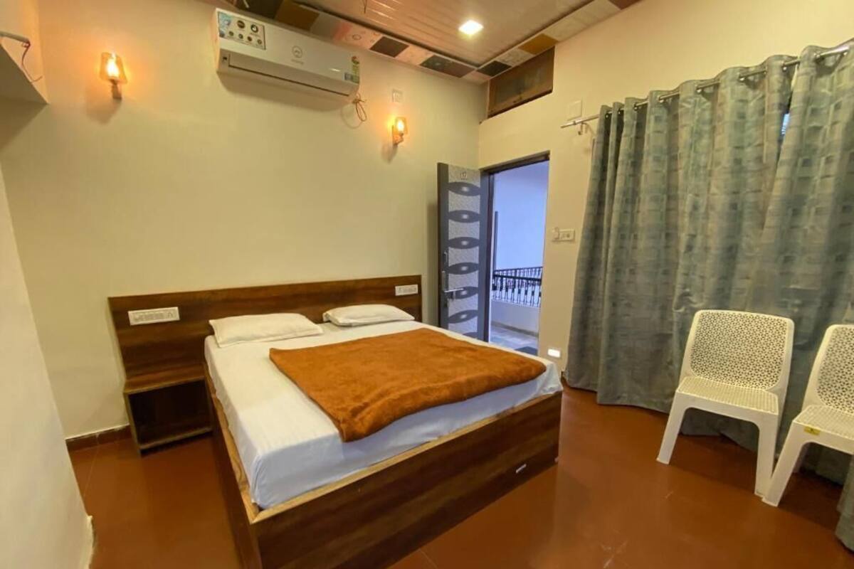Quarto com cama, cabeceira de madeira, manta marrom, cadeira branca e varanda com vista.