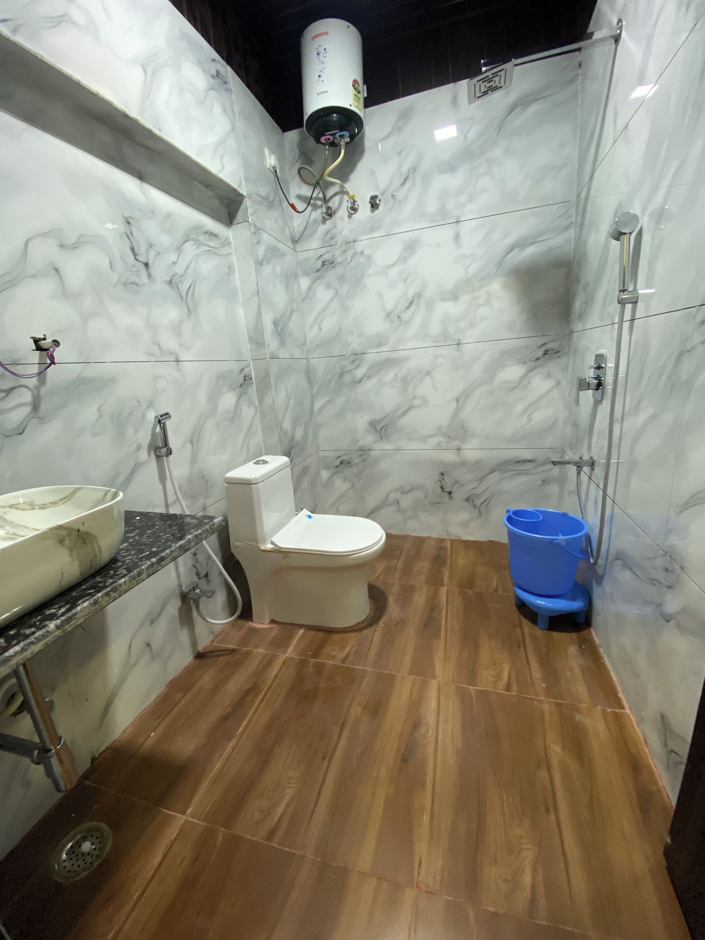 A bathroom with a toilet, sink, shower, and a blue bucket.
