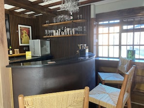 A bar area with wooden shelves, bar stools, and a refrigerator. - Pools Cottage - The Farmhouse (Coventry)