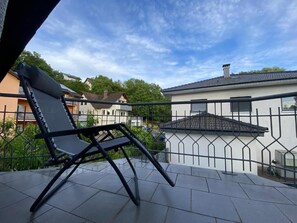 A balcony with a chair, a metal railing, and a view of houses in the background. - Pension Am Waldrand (Sinsheim)