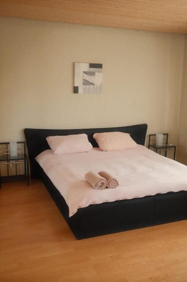 A bedroom with a black bed, two pillows, a bedside table, and a wall-mounted artwork. - Pension Am Waldrand (Sinsheim)