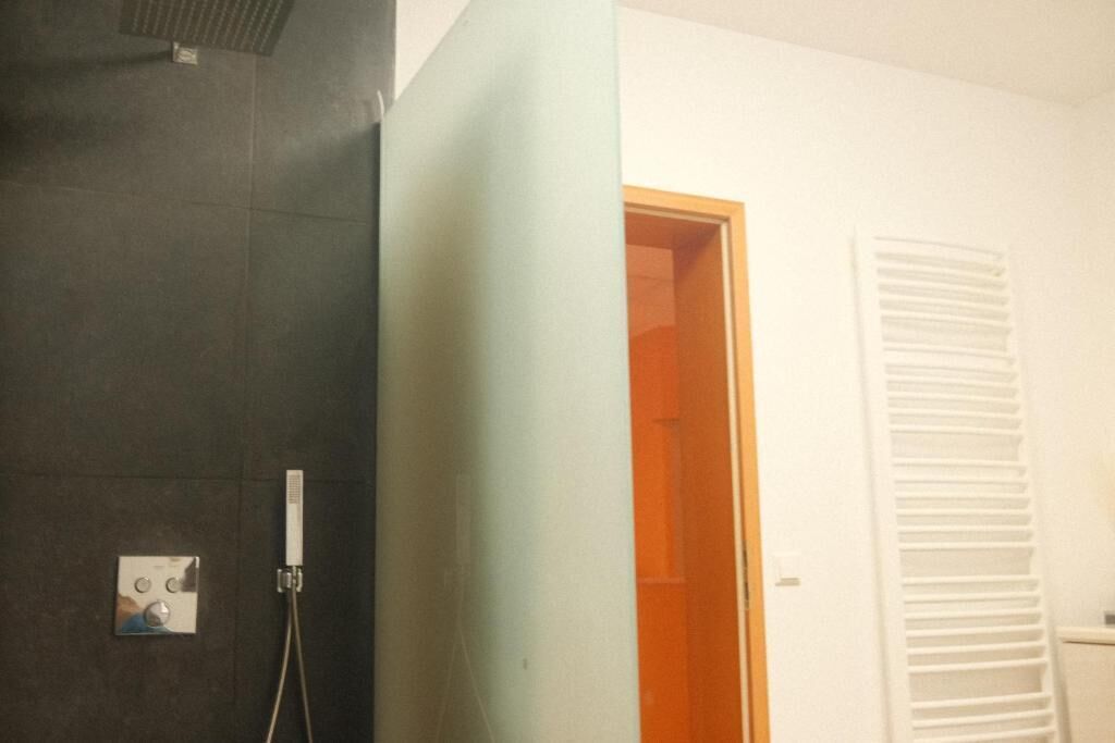 A bathroom with a shower, a towel rack, and a door leading to another room.
