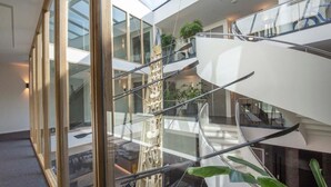 Un interior de varios niveles con barandas de cristal, una escalera central y plantas de interior.