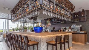Una zona de bar con encimera de mármol, varios taburetes y una selección de botellas y vasos en estantes.