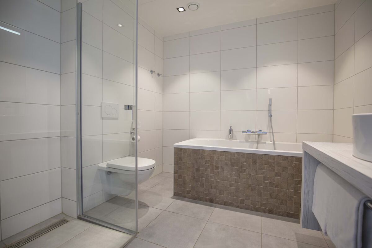Een moderne badkamer met een glazen douchecabine, een wit toilet en een badkuip met betegelde rand.