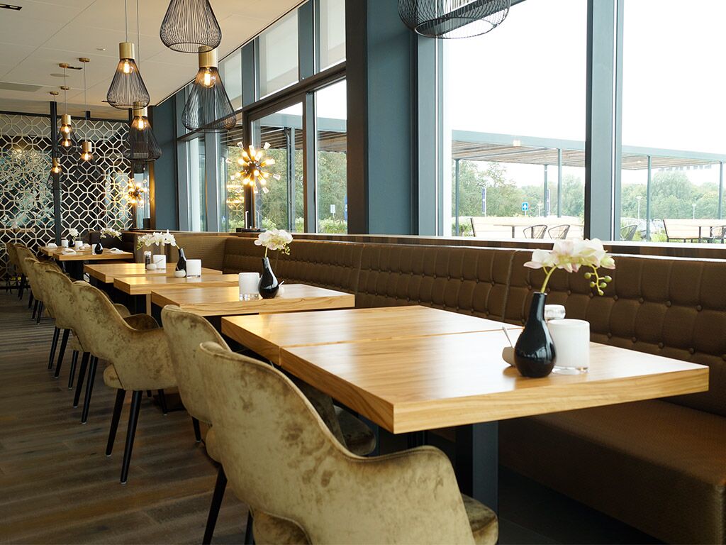 A restaurant with long wooden tables, cushioned booths, and hanging pendant lights.
