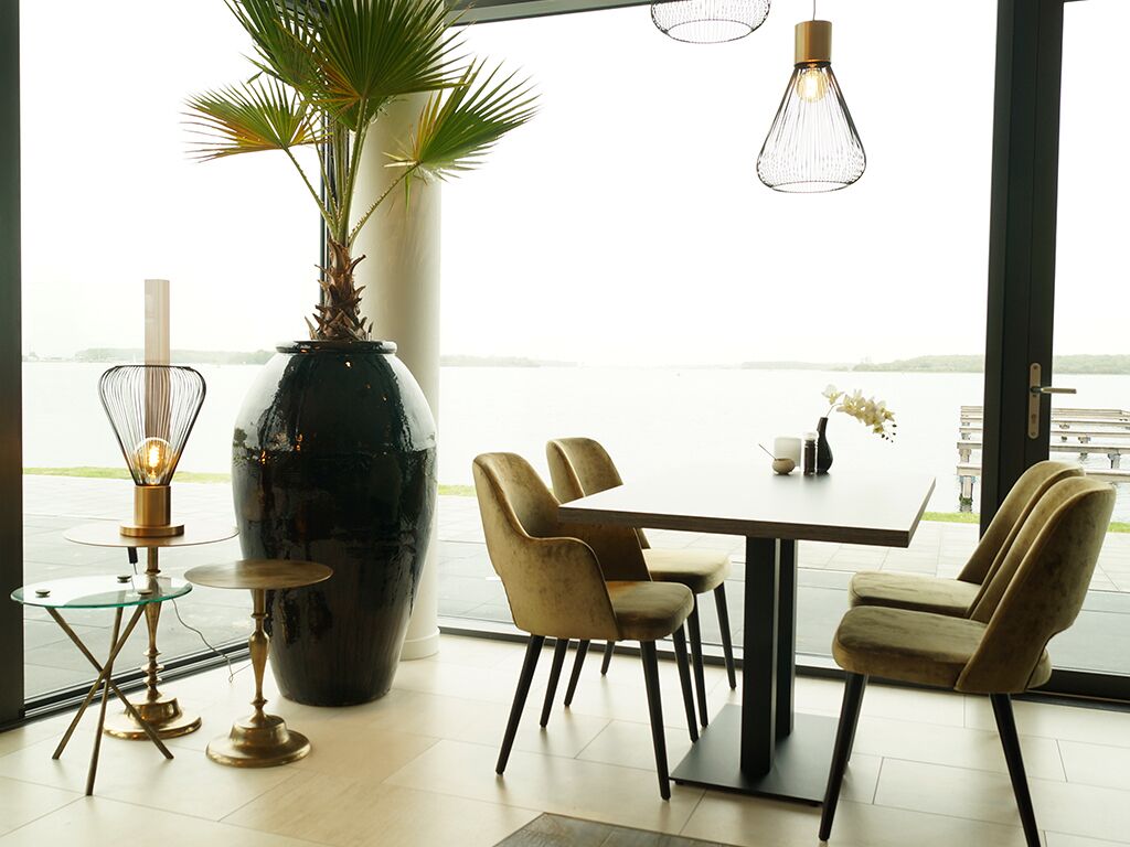 Uma sala de jantar com uma mesa, cadeiras, um vaso grande e luminárias pendentes.