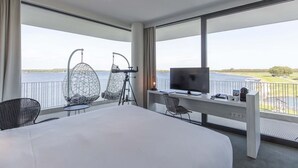 Habitación de hotel con una cama grande, dos sillones, un escritorio con televisor y un balcón con telescopio.
