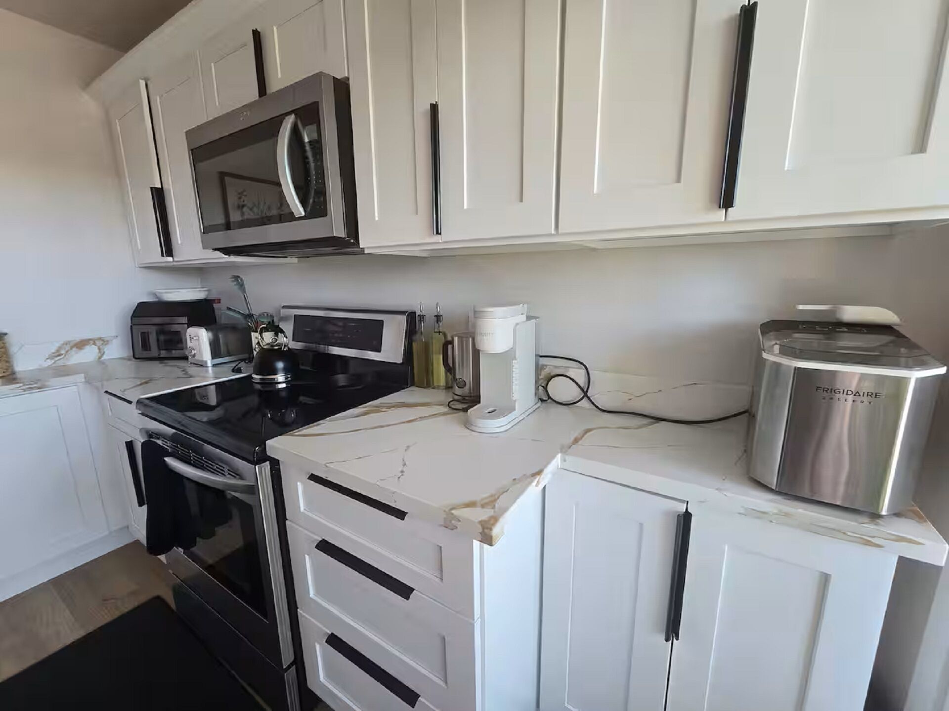 A modern kitchen with white cabinets, a microwave, a coffee maker, and a stainless steel appliance.