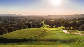 Ein Golfplatz mit sanften Hügeln, Bäumen und blauem Himmel.