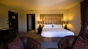 Ein Hotelzimmer mit einem Bett, zwei Nachttischen mit Lampen, einem Schreibtisch und zwei Ledersesseln.
