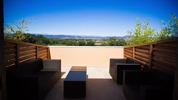Eine Dachterrasse mit Korbmöbeln, einer ebenen Fläche und einem schönen Ausblick auf ferne Berge und Grünflächen.