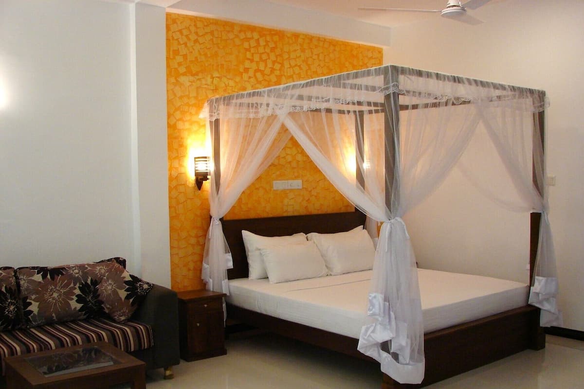 A bedroom with a four-poster bed, a sofa, a nightstand, and a wall-mounted lamp.