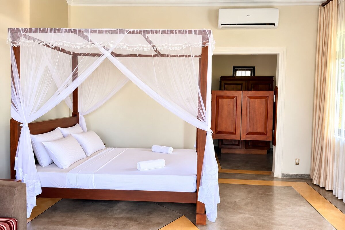 A four-poster bed with a canopy, a wooden wardrobe, and a tiled floor.