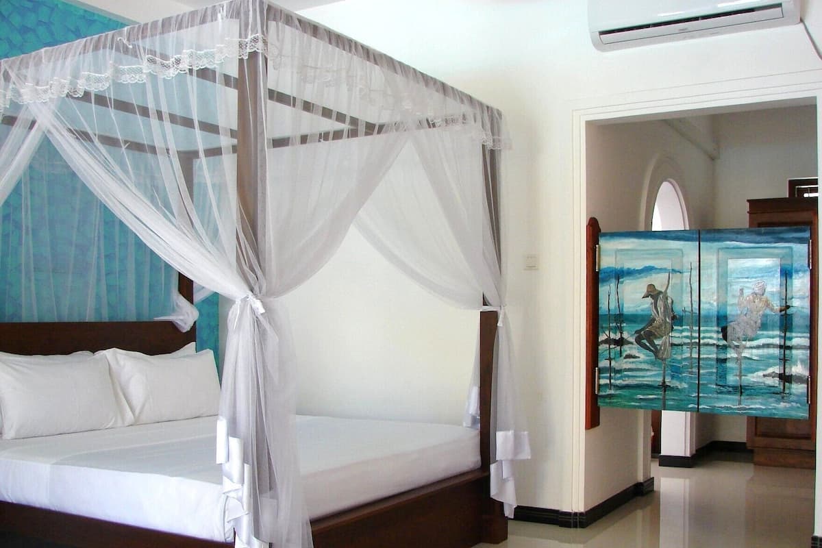 A bed with a canopy, a painting on the wall, and a hallway leading to another room.