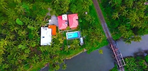 An aerial view of a property with a swimming pool, a bridge, and a small building with a red roof.