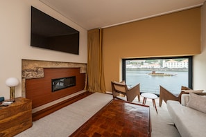 A modern living room with a fireplace, a television, and a view of a river with boats. - Premium 2BR Duplex Douro River View (Vila Nova de Gaia)