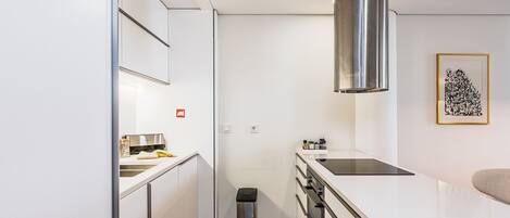 Una cocina moderna con armarios blancos, una campana extractora de acero inoxidable, una placa de inducción negra y un pequeño contenedor de basura.