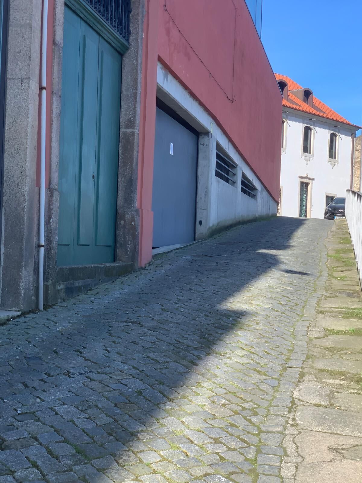 A cobblestone street with a building featuring a green door and a garage.