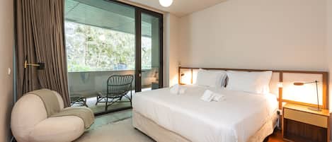 Une chambre moderne avec un grand lit, une chaise, une table de chevet et une vue sur l’extérieur.