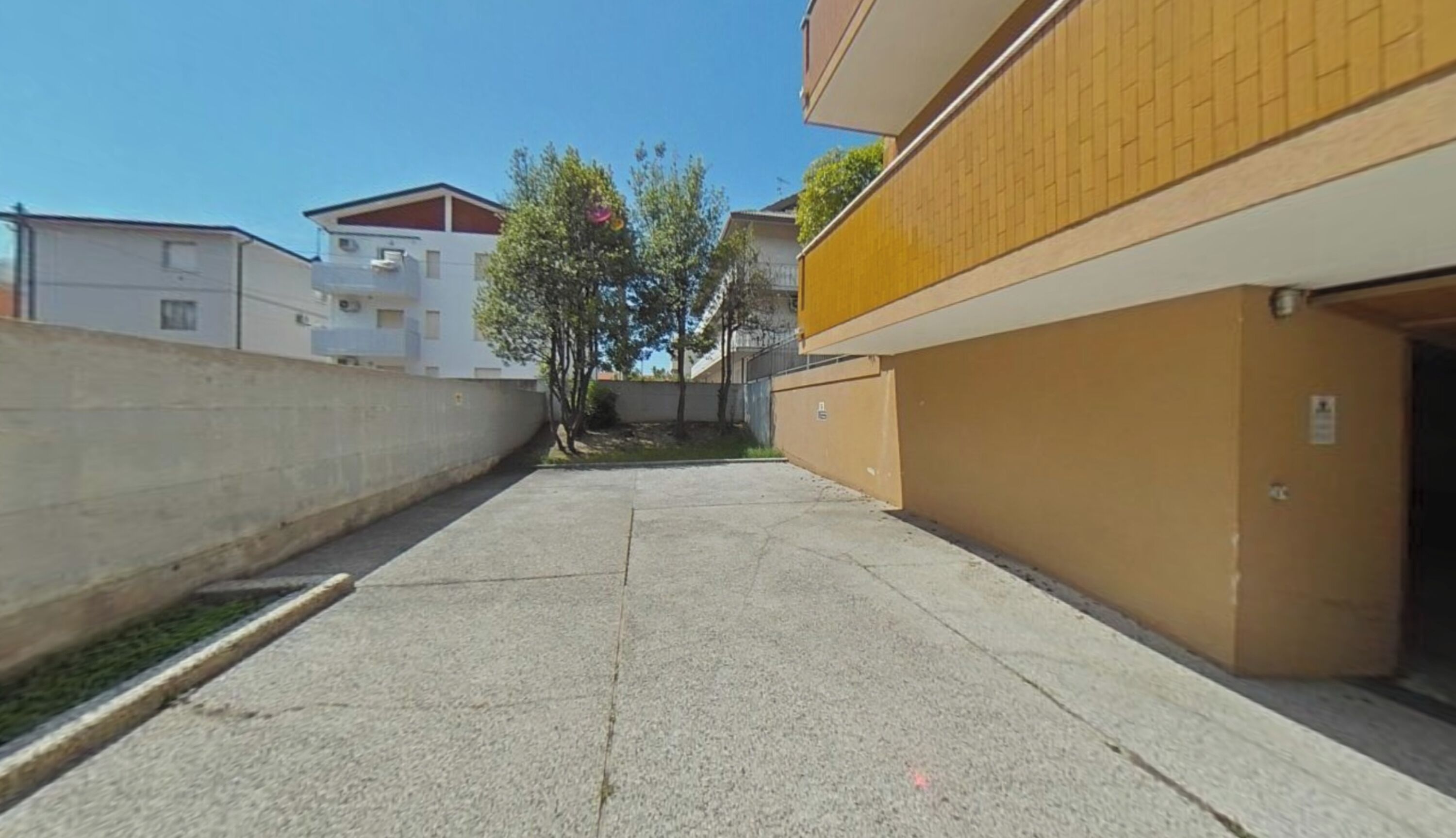 Un estrecho callejón entre edificios, con un árbol en el centro y un cielo despejado arriba.