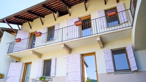 Un immeuble de deux étages doté de balcons, de volets et d’une table avec des chaises à l’extérieur.