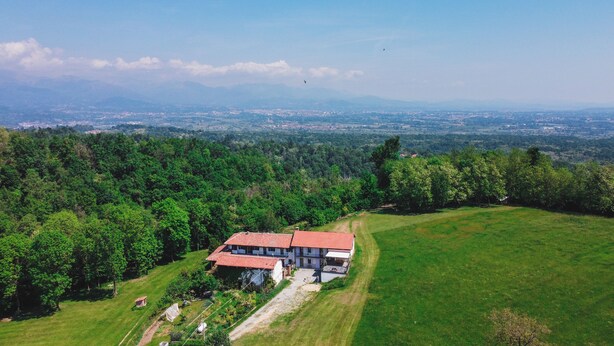 Une maison avec un toit rouge, entourée d’un champ verdoyant et d’une forêt dense.