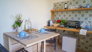 Une cuisine compacte équipée d’un four à micro-ondes, d’un grille-pain et d’un petit réfrigérateur. On y trouve une table à manger avec des sets de table et un vase de fleurs.