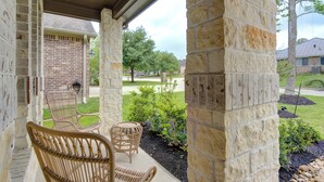 A covered porch with wicker chairs, a stone pillar, and a brick building in the background. - Sleeps 18 5BR Walden Home Near Lake Conroe & Margaritaville (Montgomery)