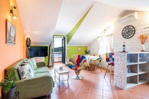 A living room with a sofa, a coffee table, a colorful chair, a dining table with chairs, a TV, and a clock on the wall. - Antique Villa, Panoramic view with Pool (Dubrovnik)