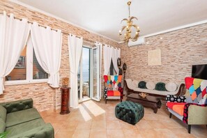 A living room with a stone wall, a green sofa, a colorful armchair, a wooden coffee table, and a chandelier. - Antique Villa, Panoramic view with Pool (Dubrovnik)