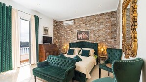 Ein Schlafzimmer mit Steingemäuer, einem Bett mit grüner Bettwäsche, einer grünen Couch, einem Sessel und einem Fernseher.