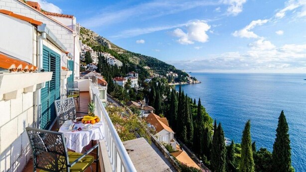 Ein Balkon mit Tisch, Stühlen und Blick auf das Meer sowie Hügelhäuser.