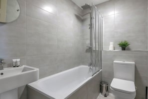 A modern bathroom with a bathtub, toilet, sink, and a small potted plant. - Peregrine House  (Nottingham)