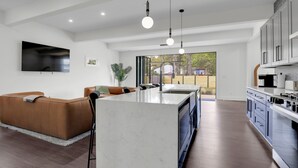 Una cucina moderna con isola centrale, illuminazione a sospensione e un grande televisore a parete.