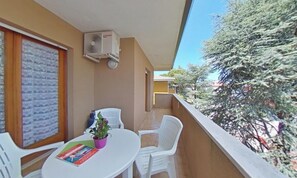 A balcony with a table, chairs, a potted plant, and an air conditioning unit. - Practical and Spacious Flat (Lignano Sabbiadoro)