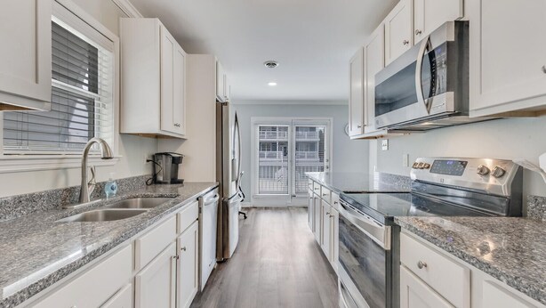 Una cocina moderna con armarios blancos, encimeras de granito y electrodomésticos de acero inoxidable, y vistas al exterior.