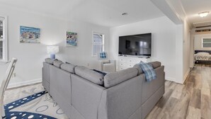 Una sala moderna con un sofá seccional gris, un televisor de pantalla plana y un comedor con una mesa y sillas blancas.