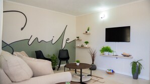 Ein Wohnzimmer mit einer Couch, einem Couchtisch, einem Fernseher und Regalen mit Pflanzen.