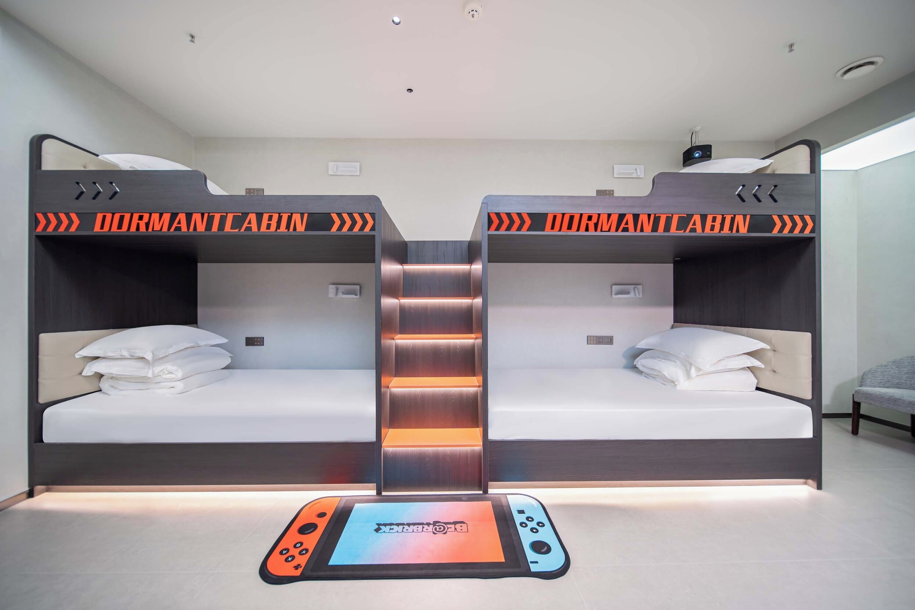 Habitación tipo dormitorio con dos camas, una escalera central y una consola de videojuegos en el suelo.