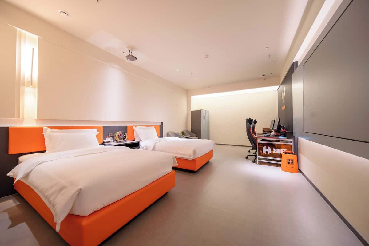 A hotel room with two beds, a desk, a chair, a TV, and a minibar.
