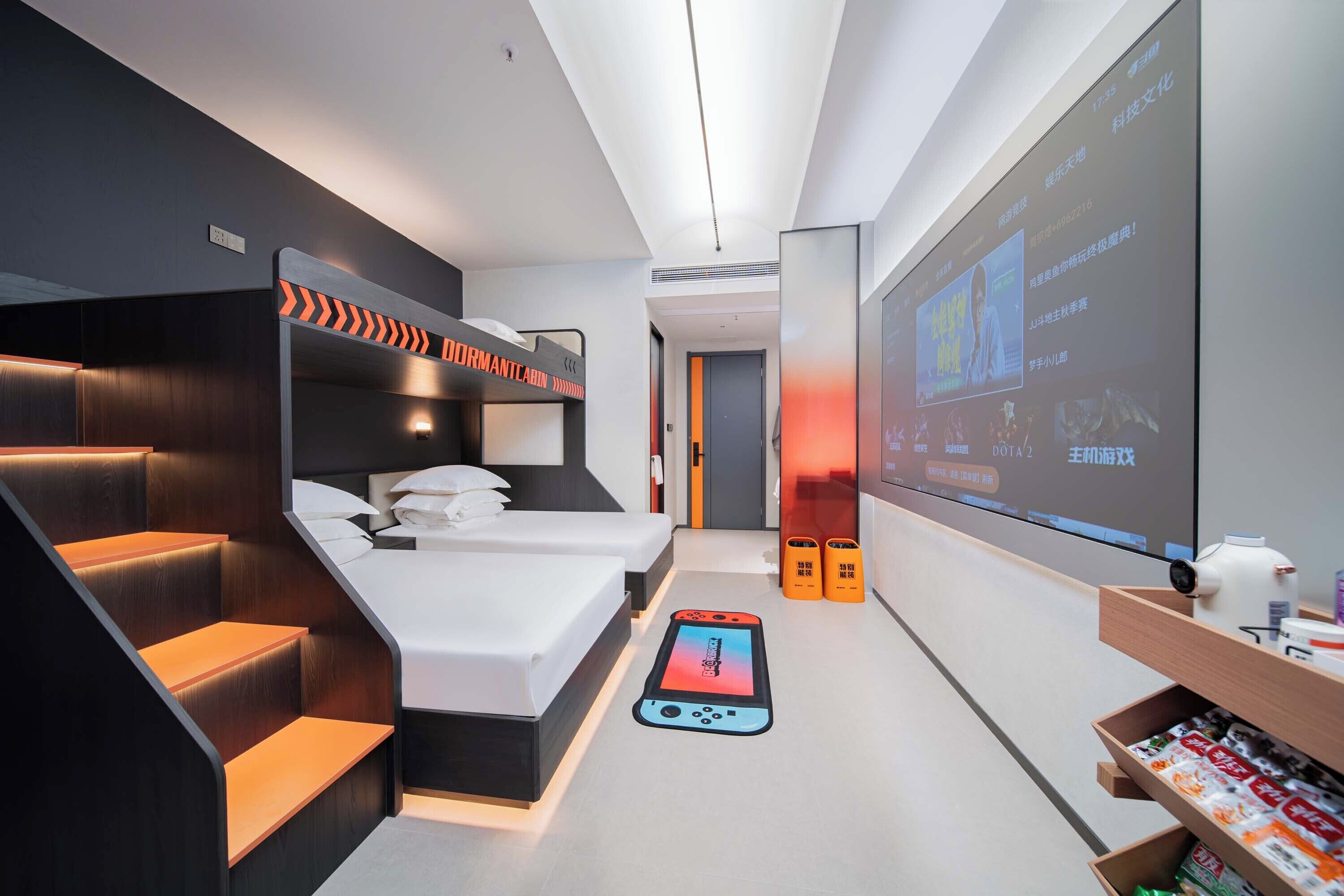 Una habitación de hotel moderna con una cama litera, un teléfono inteligente en el suelo, una pantalla de proyector y un estante de madera con objetos.