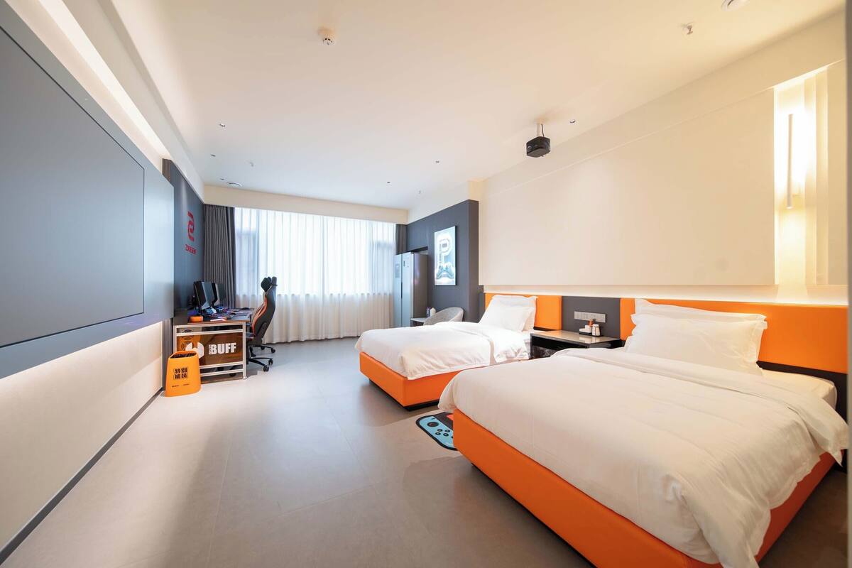 A hotel room with two beds, a desk, a chair, and a large window with curtains.