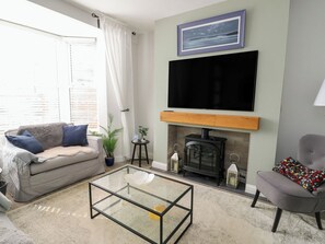 A living room with a sofa, a glass coffee table, a fireplace, a television, and a chair. - Bryn Y Mor (Beaumaris)