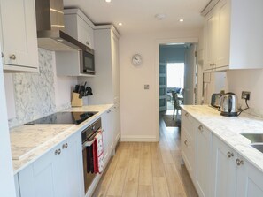 A modern kitchen with white cabinetry, a microwave, an oven, and a clock on the wall. - Bryn Y Mor (Beaumaris)