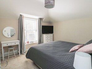 A bedroom with a bed, a dresser, a mirror, a television, and a window with blinds. - Bryn Y Mor (Beaumaris)
