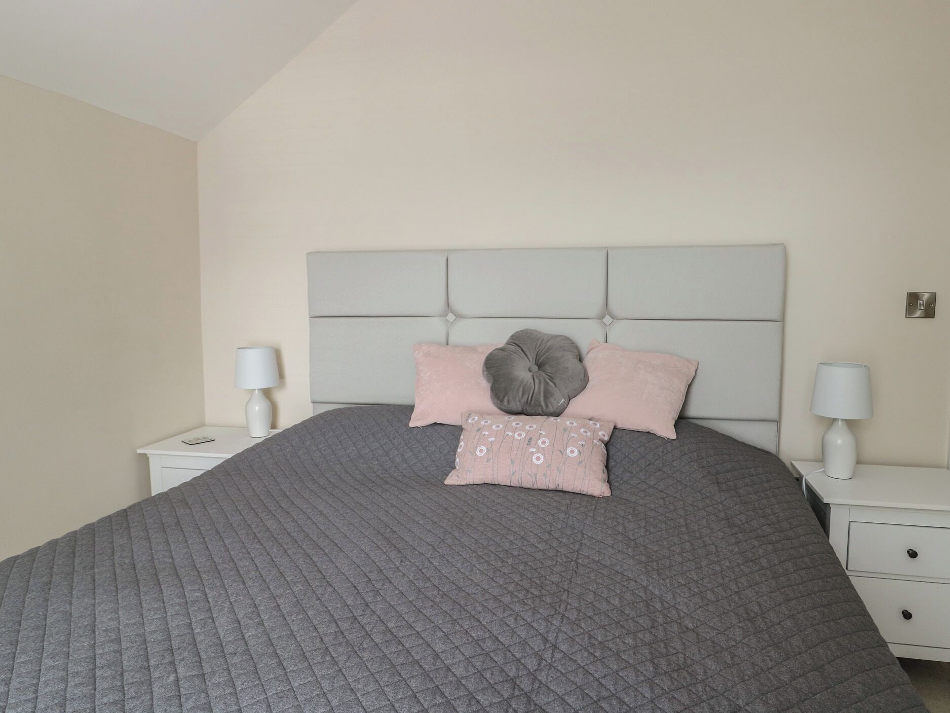 A neatly made bed with a grey quilt, a headboard, and two bedside tables with lamps.